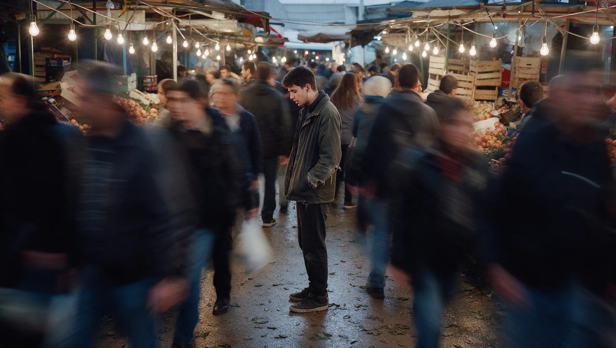 A young man stands still and speaks quietly while a market crowd blurs around him
