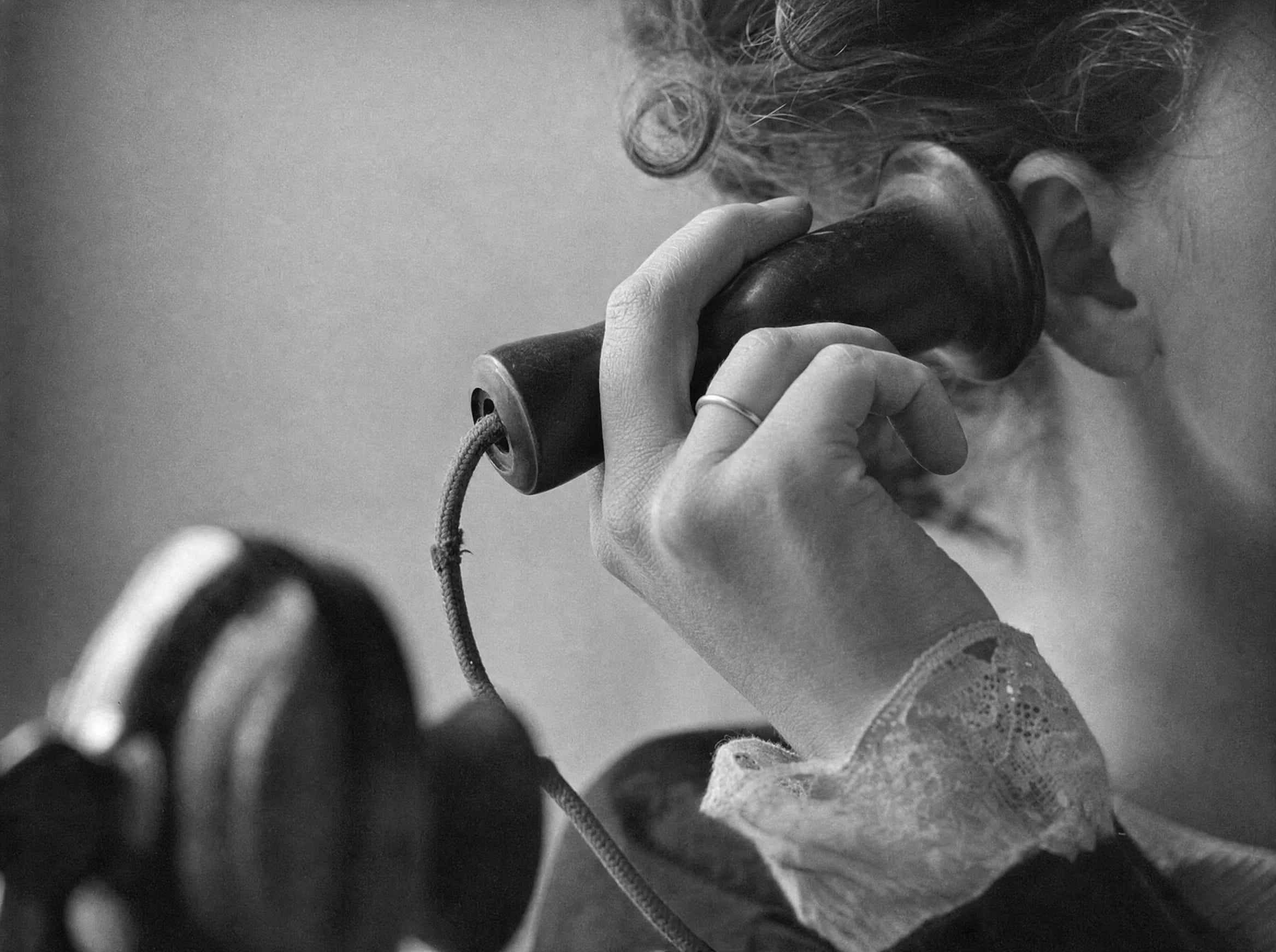 A woman holds a candlestick telephone earpiece to her ear