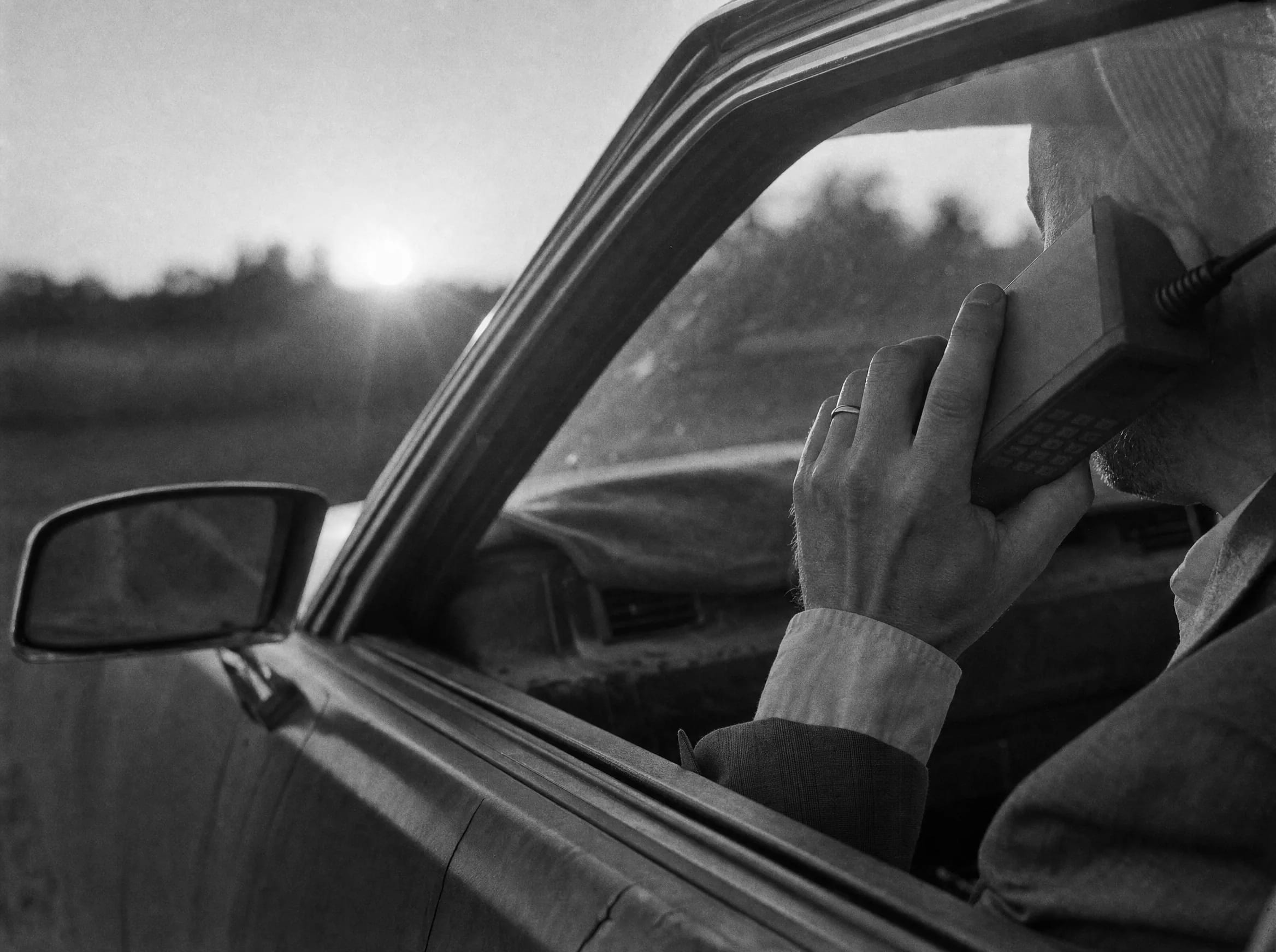 A man in a car holds a brick-sized early mobile phone to his ear