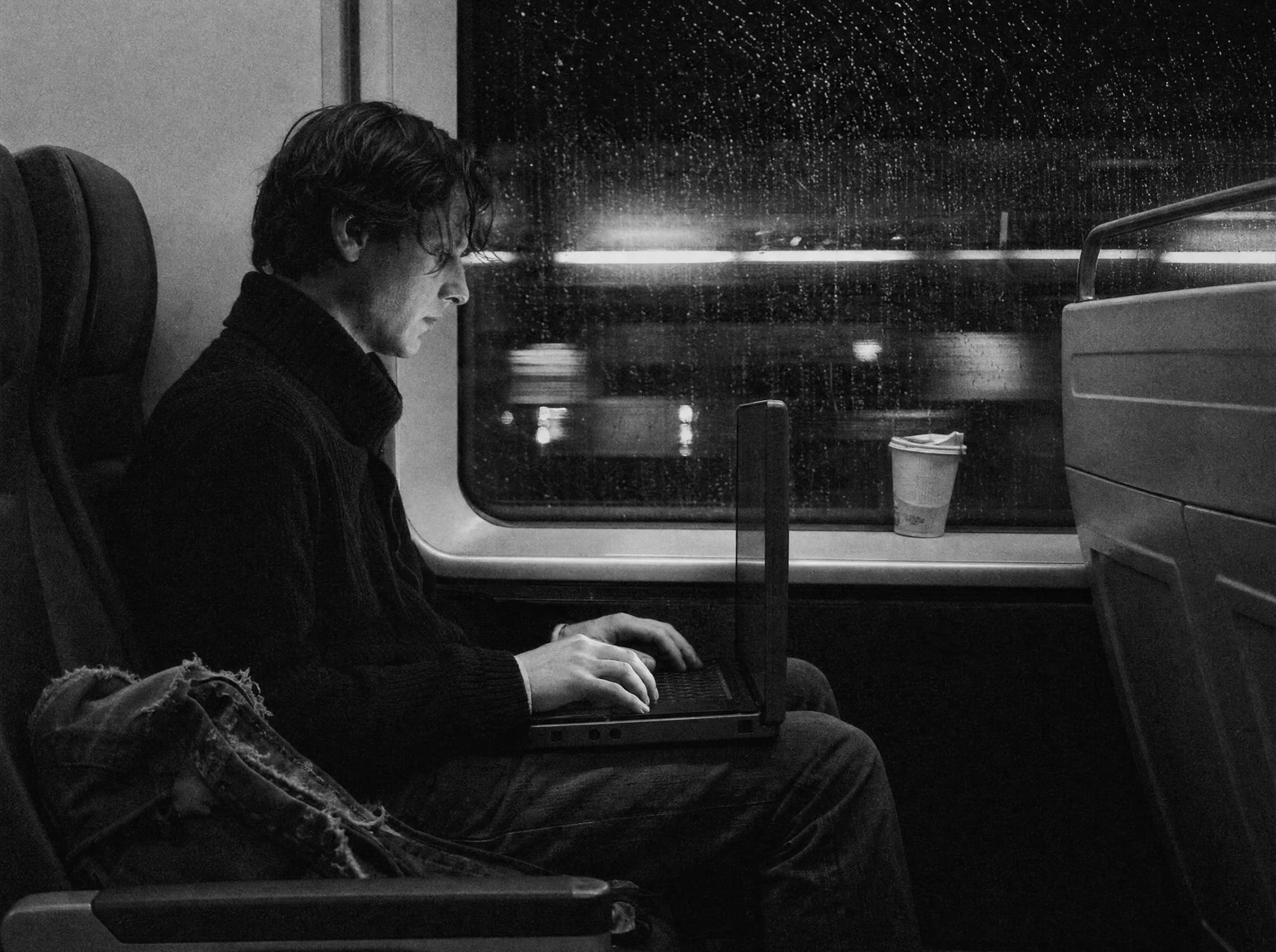 Hands typing on a laptop balanced on knees on a night train