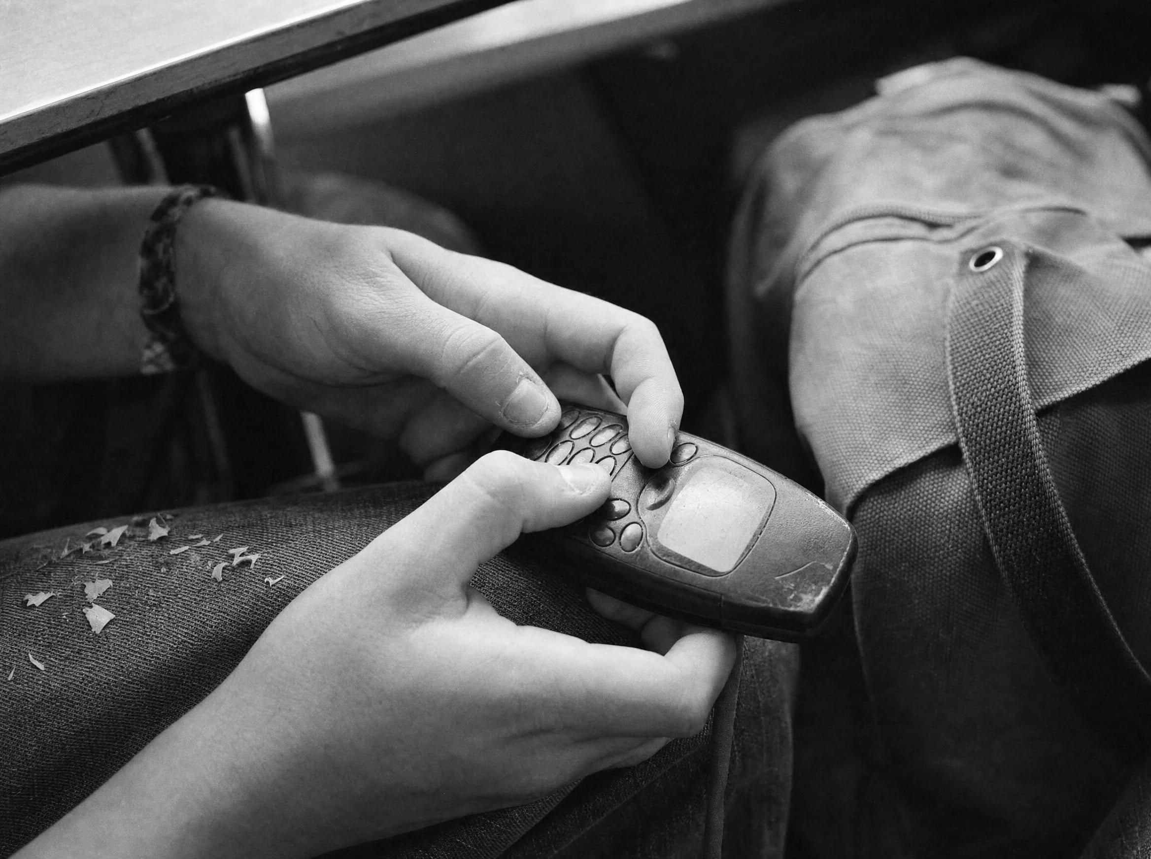 Two thumbs pressing the keys of a small mobile phone under a school desk